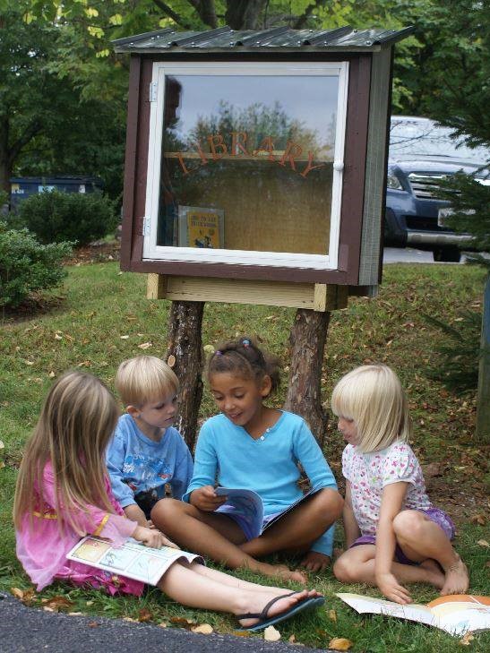 Four children sitting beneath the little free library looking through books.